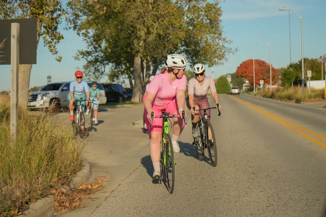 Riders in pink and dusty rose chatting on a road lined with autumn trees