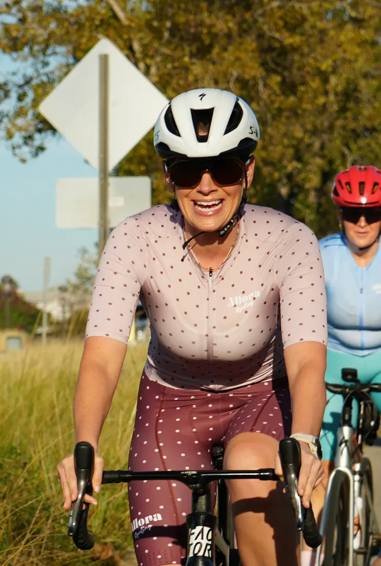 A rider in the dusty-rose polka-dot Allora kit smiling toward the camera