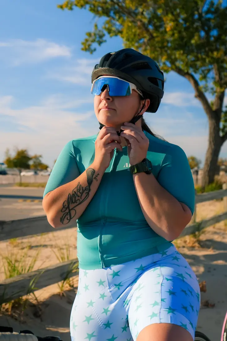 A rider in the teal jersey buckling her helmet