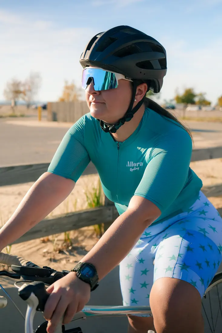 A rider in the teal jersey riding with sand dunes behind her